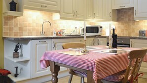 Una cucina con mobili bianchi, un forno a microonde, un lavello e un tavolo apparecchiato con tovaglia a quadretti rossi e bianchi.
