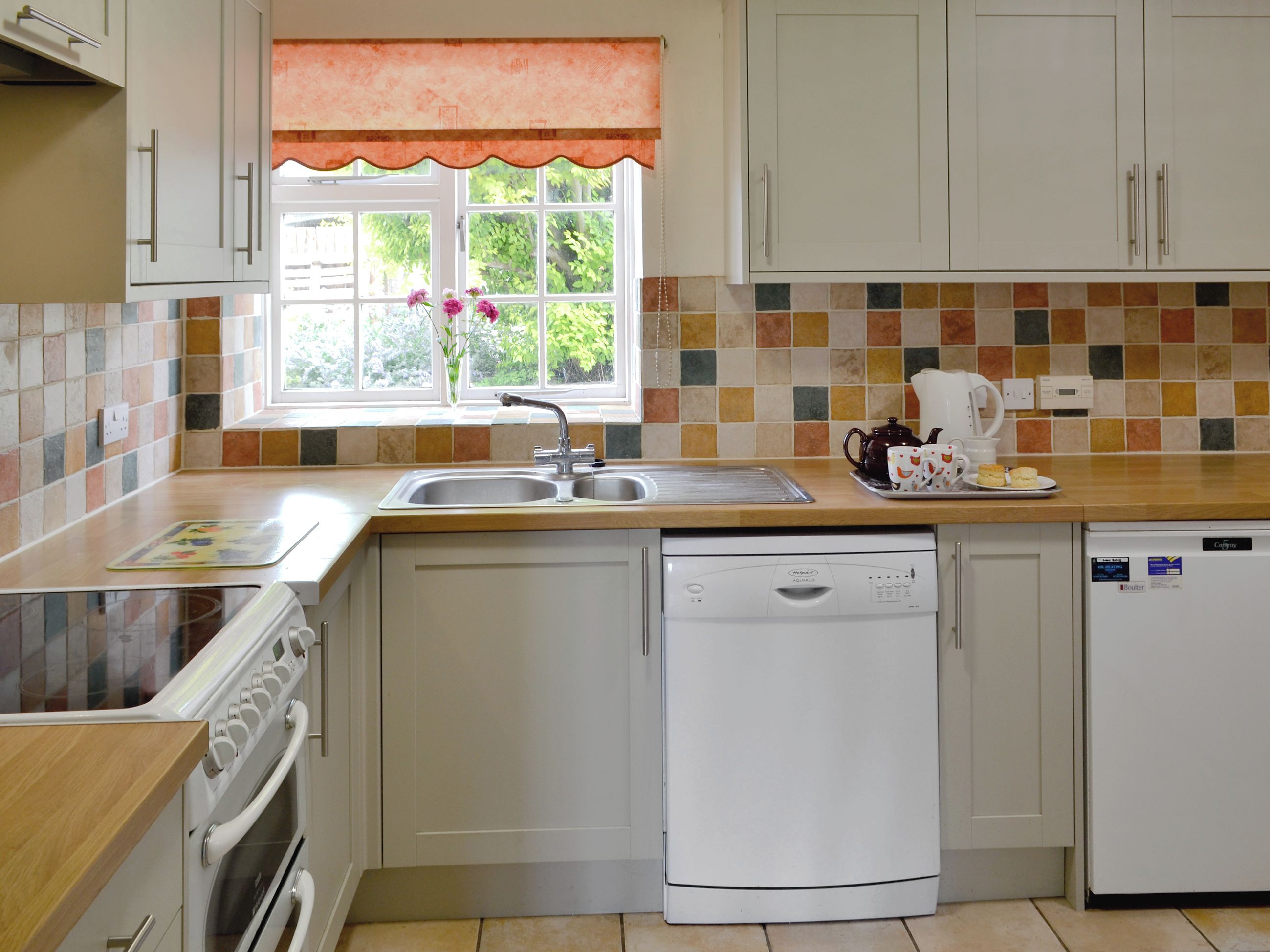 A kitchen with a dishwasher, oven, and a window with a view of greenery.