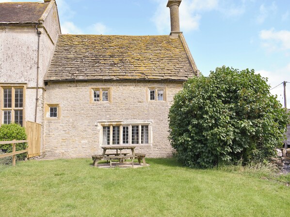 A stone house with a tiled roof, a wooden fence, and a large tree in the yard.