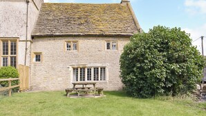 Une maison en pierre avec un toit en tuiles, une clôture en bois et un grand arbre dans la cour.
