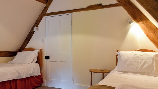Un dormitorio con dos camas individuales, techo de madera, una puerta blanca y una pequeña mesa de madera.