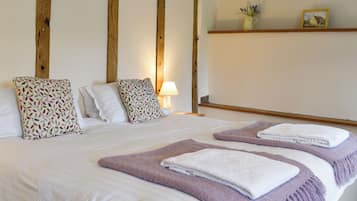 A bed with white linens, two decorative pillows, a bedside lamp, and a shelf with a picture and a vase.