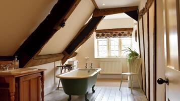 A bathroom with a clawfoot bathtub, wooden beams, a window with a leaf-patterned valance, and a radiator.