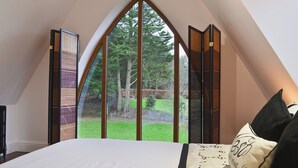 Een slaapkamer met een groot raam, een bed en uitzicht op een tuin.