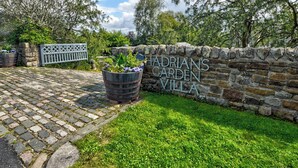 A stone wall with the text "Hadrian's Garden Villa" and a wooden bench. - Hadrians Garden Villa (Henshaw, near Haltwhistle)