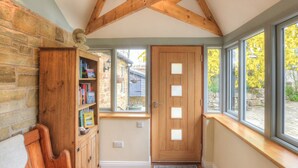 A cozy room with a wooden bench, a bookshelf, a door with frosted glass panels, and large windows offering a view of the outside. - Hadrians Garden Villa (Henshaw, near Haltwhistle)