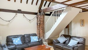 Uma sala de estar com dois sofás de couro, uma mesa de centro de madeira e uma escada que dá para um andar superior.