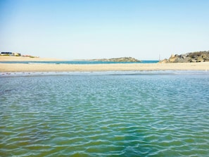 Une plage à l’eau claire, avec un rivage sablonneux et des affleurements rocheux.
