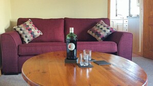 A wooden coffee table with a bottle of gin and two glasses in front of a red sofa with patterned pillows.