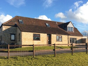 A stone building with a tiled roof, multiple windows, and a fenced area in front. - 4 bedroom accommodation in Hawkesbury Upton (Hawkesbury Upton)
