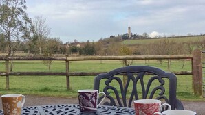 A metal table with four patterned mugs, a chair, and a view of a green field and a distant building.