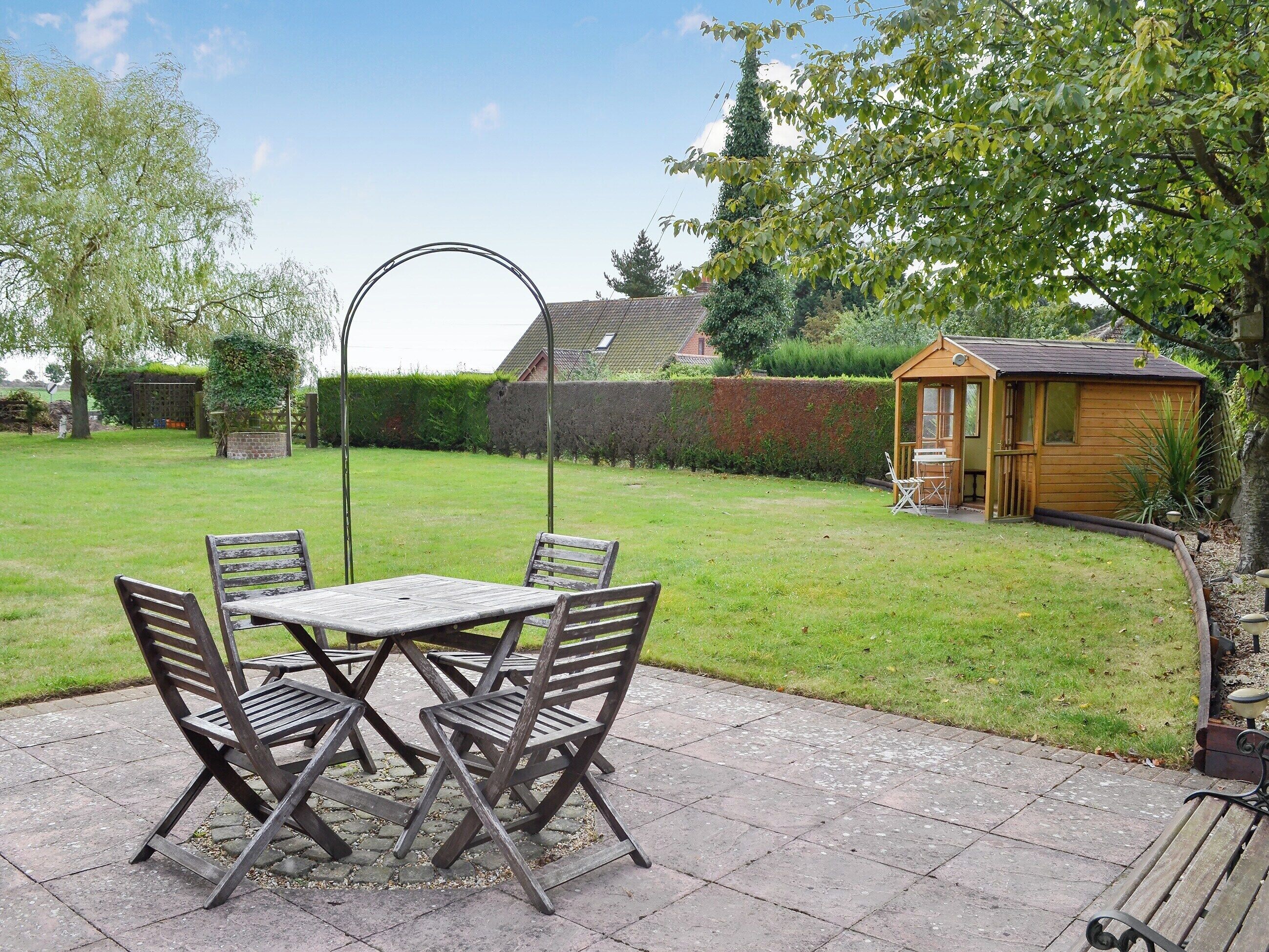 A patio with a table and chairs, a wooden shed, and a well-maintained lawn.