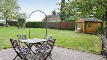 A patio with a table and chairs, a wooden shed, and a well-maintained lawn.