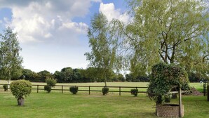 A grassy field with a wooden fence, trees, and a brick structure. - 1 bedroom accommodation in Polstead (Polstead)