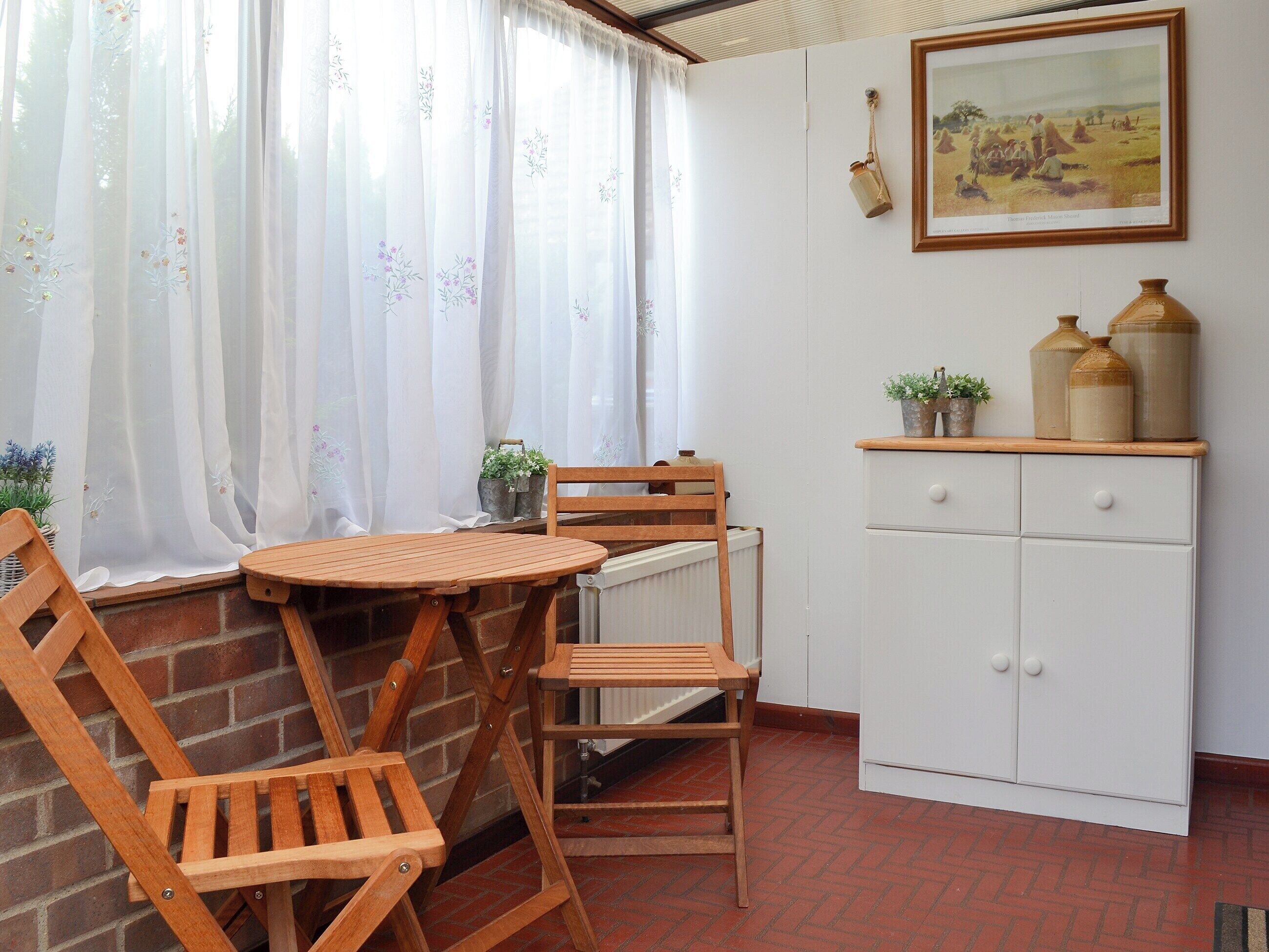 A small room with a wooden table and chairs, a white cabinet, and a window with sheer curtains.