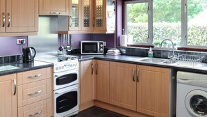 A modern kitchen with wooden cabinets, a built-in oven, a microwave, and a washing machine. - 1 bedroom accommodation in Polstead (Polstead)
