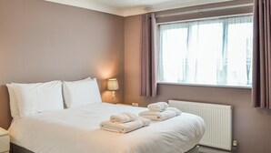 Un lit bien fait, avec du linge de lit et des serviettes blanches, une lampe de chevet et une fenêtre avec des rideaux.