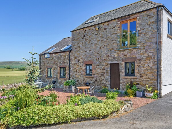 A stone house with a patio, outdoor seating, and a view of the countryside. - New Park Farm - Church Cottage (near Keswick)