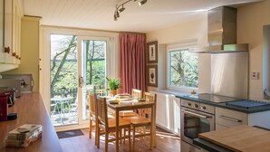 A kitchen with wooden cabinets, a dining table with chairs, a built-in oven, and a large window with a view of trees. - A superior detached spacious cottage in an idyllic, truly rural location. (Dockray)