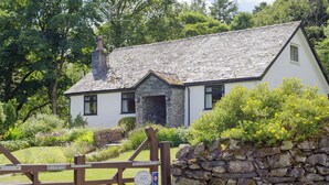 A stone cottage with a white exterior, a stone chimney, and a wooden gate. - A superior detached spacious cottage in an idyllic, truly rural location. (Dockray)