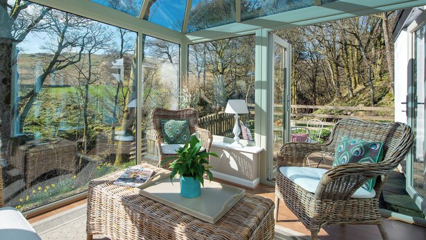 A conservatory with wicker furniture, a table, and a potted plant. - A superior detached spacious cottage in an idyllic, truly rural location. (Dockray)