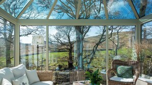 A conservatory with wicker furniture, a potted plant, and a view of a green landscape. - A superior detached spacious cottage in an idyllic, truly rural location. (Dockray)