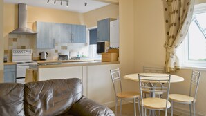 A compact kitchen with modern appliances, a dining area with a round table and chairs, and a sofa in the foreground. - 2 bedroom accommodation in Keswick (Keswick)