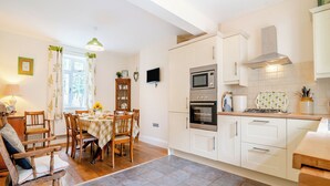 A kitchen with white cabinets, a dining table with chairs, a built-in oven, and a TV mounted on the wall.