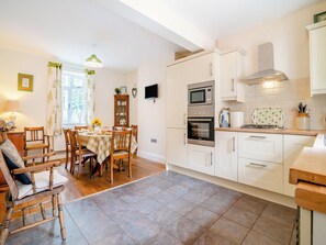 A kitchen with white cabinets, a dining table with chairs, a built-in oven, and a TV mounted on the wall.
