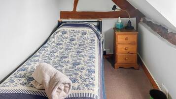 A bedroom with a bed, a nightstand, a lamp, a wooden dresser, and a green trash can.