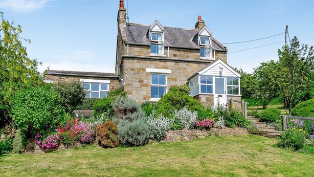 A two-story stone house with a garden in front.