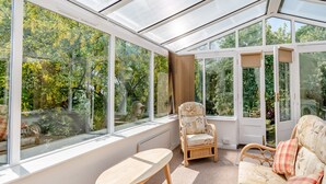 A conservatory with large windows, wicker furniture, and a view of trees.