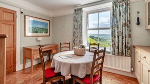 A dining area with a round table, chairs, a wooden cabinet, a framed picture on the wall, and a window with curtains.