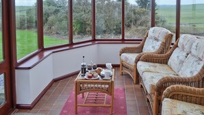 Een oranjerie met rieten meubilair en een gedekte tafel voor thee, met uitzicht op een groen landschap.
