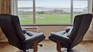 Een kamer met twee zwarte leren stoelen gericht op een groot raam met uitzicht op een grasveld en een waterpartij.