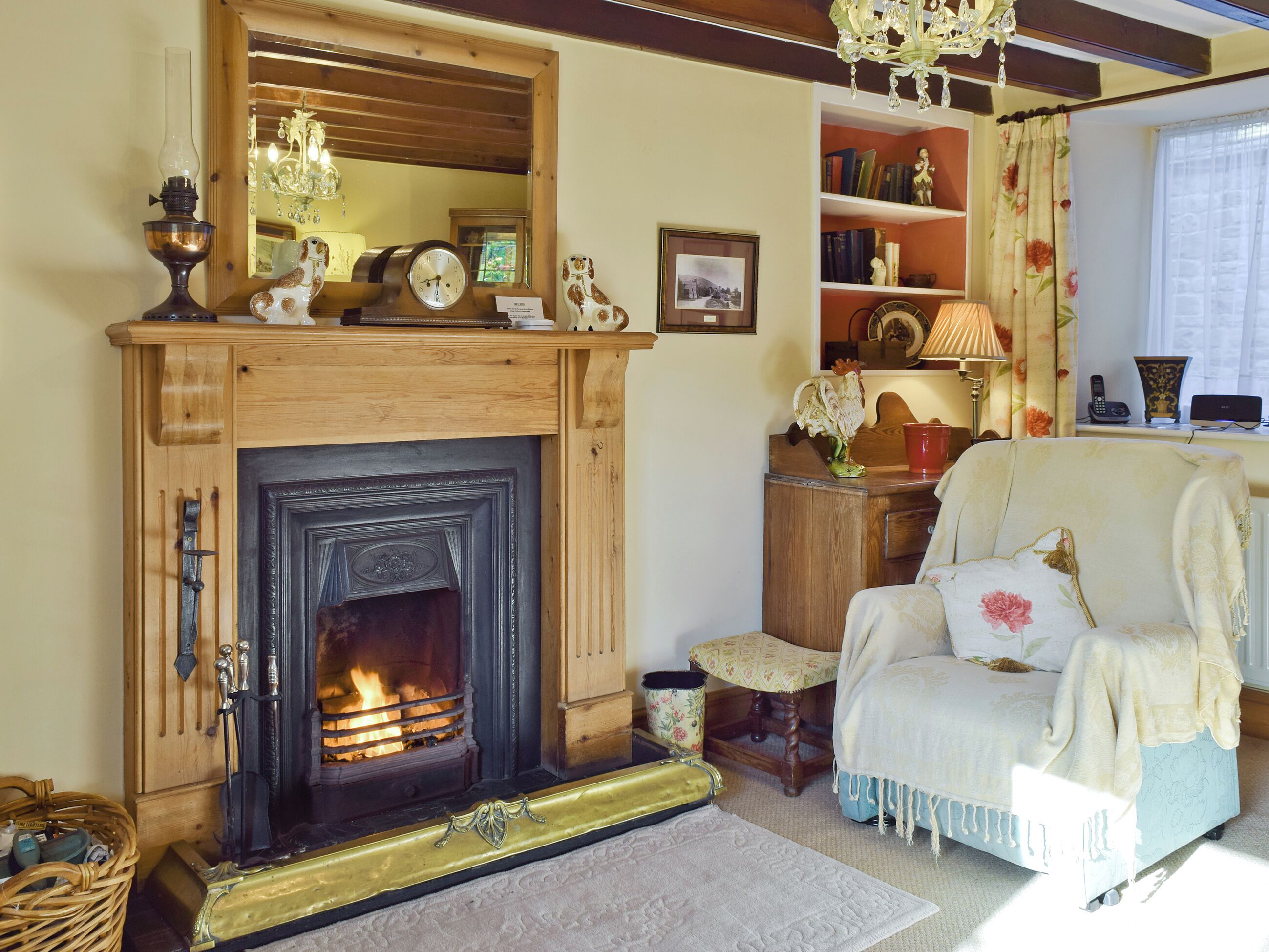 Ein gemütliches Wohnzimmer mit Kamin, Holzmöbeln, einer Bücherwand und einem blumengemusterten Sofa.
