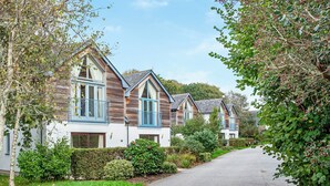 A row of two-story houses with wooden exteriors and blue window frames, a paved driveway, and lush greenery. - 2 bedroom accommodation in Carnon Downs, near Truro (Carnon Downs, near Truro)
