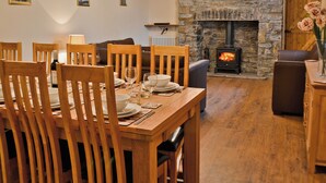 Un comedor con sillas de madera y una mesa dispuesta para una comida, una chimenea de piedra con un televisor montado encima, y un sofá al fondo.