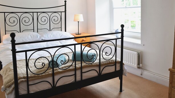 Ein Bett mit Metallgestell, ein Nachttisch mit Lampe und ein Fenster mit Blick ins Grüne.