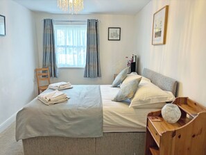 A bedroom with a bed, a chair, a bedside table, a vase, and a window with curtains. - A ground floor apartment with level access, in Keswick. (Keswick)