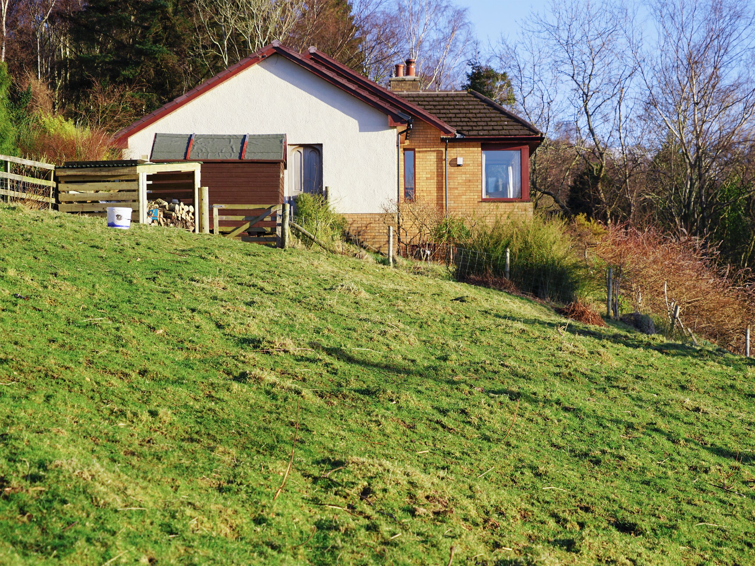 A house with a garage, a fenced yard, and a grassy hill.