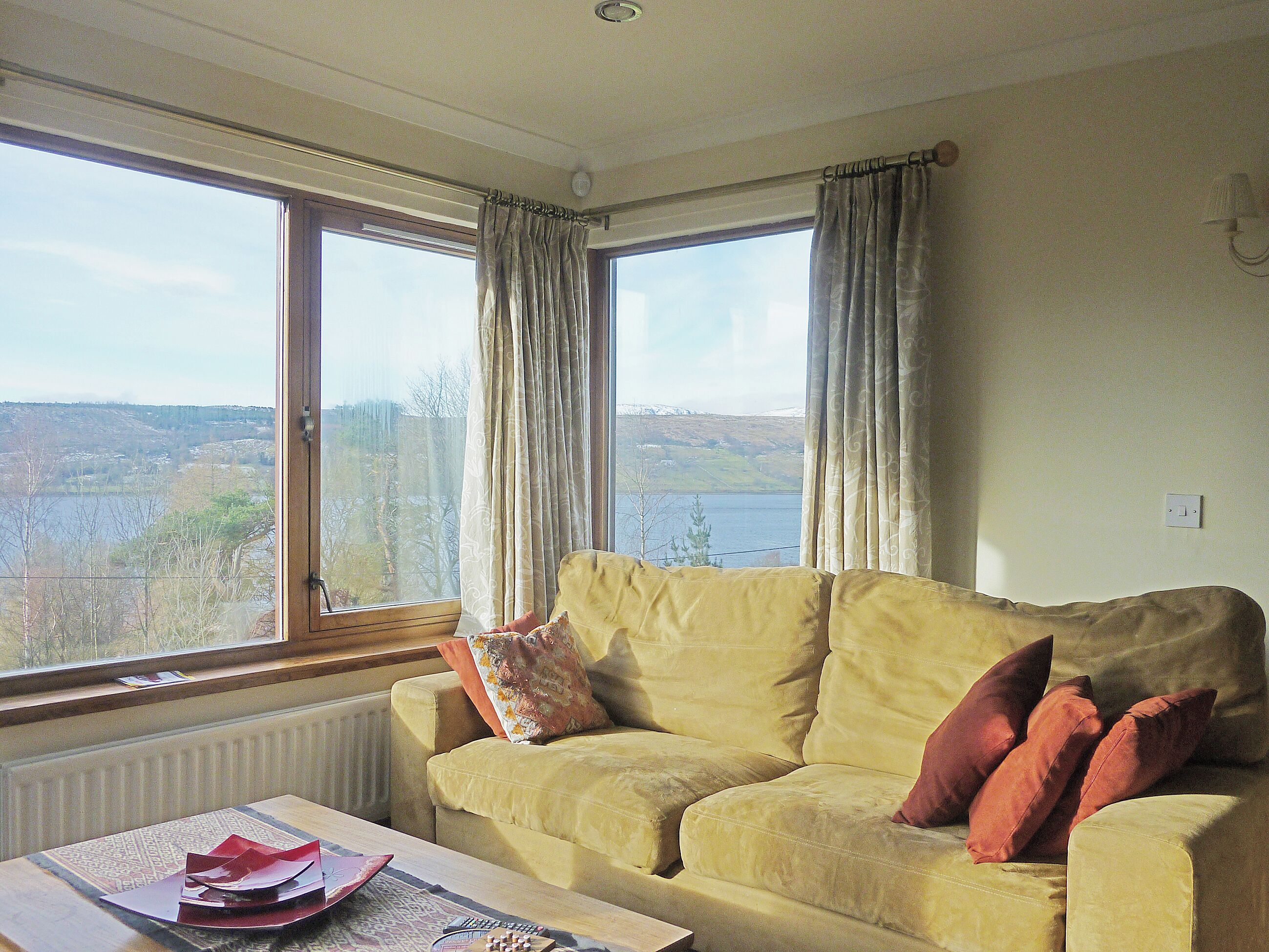 A room with a sofa facing a large window overlooking a lake and hills.