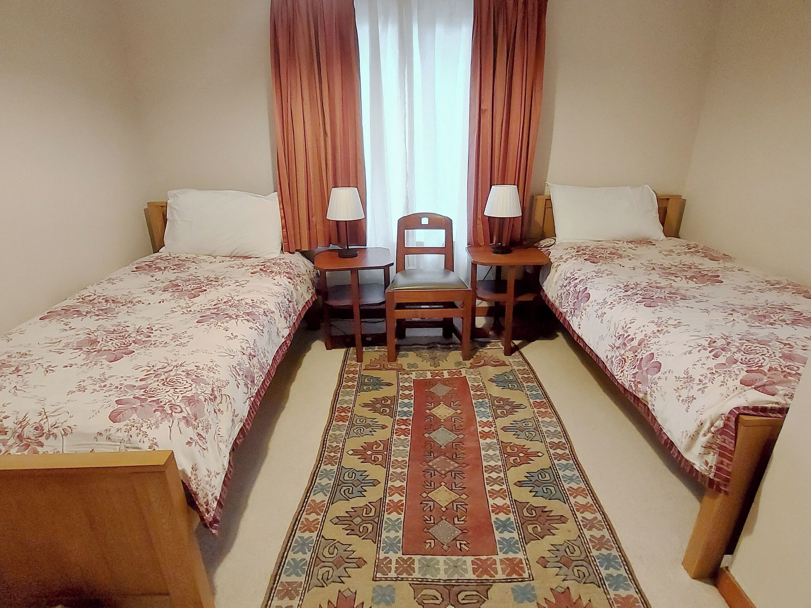 Une chambre avec deux lits simples, une petite table avec une chaise et un tapis à motifs.