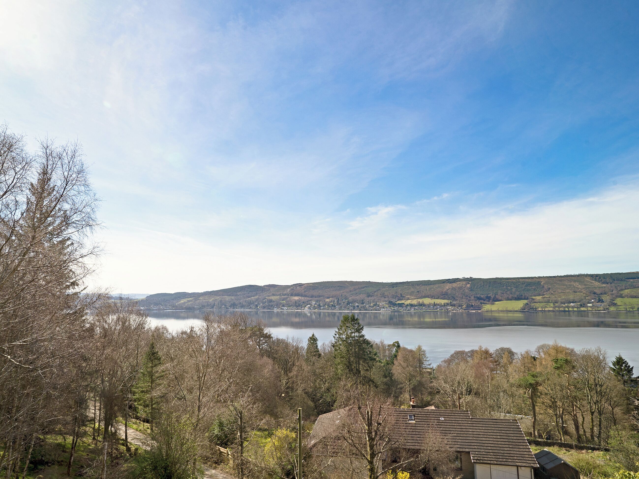 A lakeside view with a house in the foreground and hills in the background.