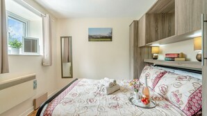 Ein Schlafzimmer mit Bett, Fenster, Heizkörper, Spiegel und einem Regal mit Büchern und Lampen.