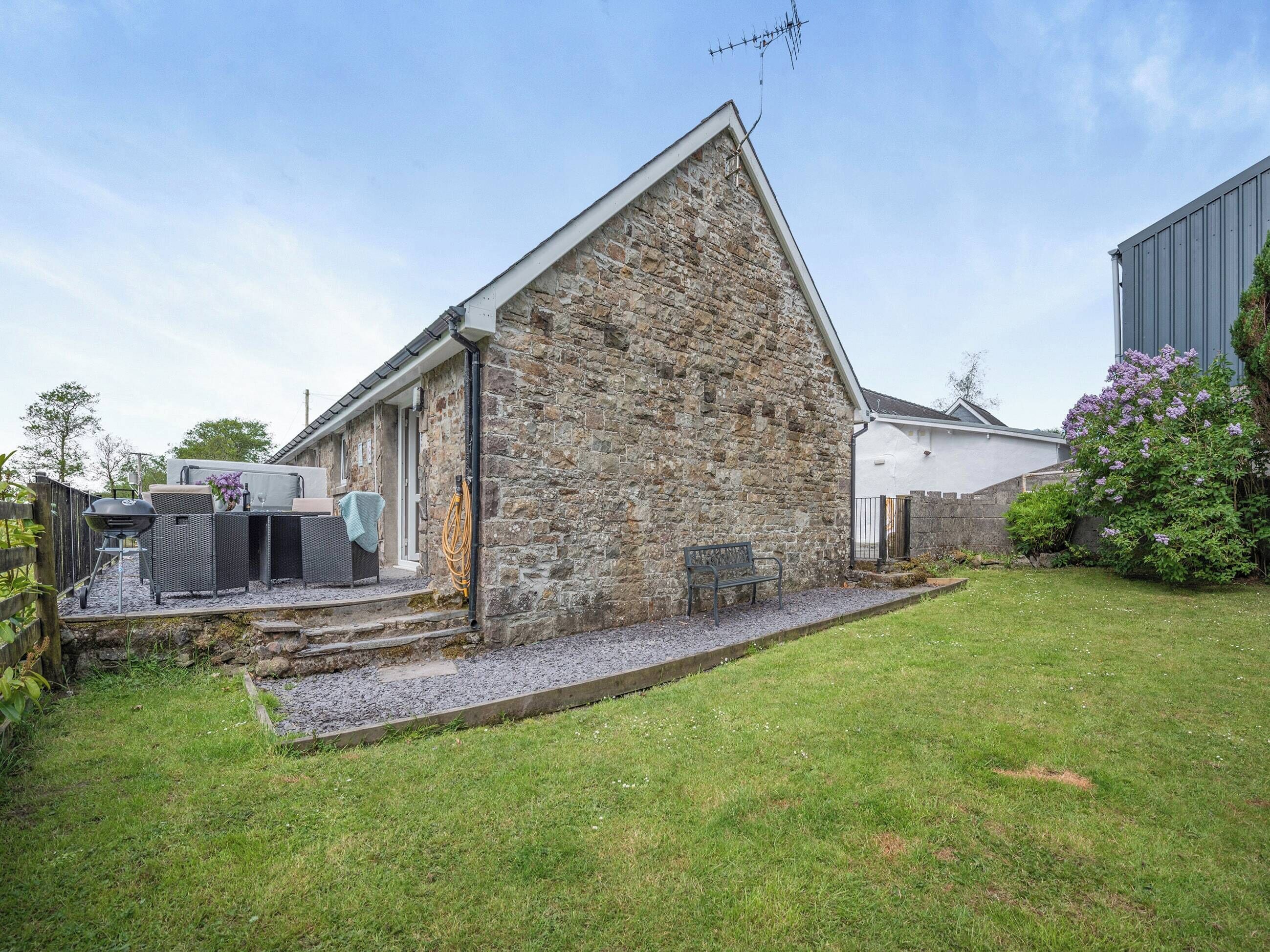 Une maison en pierre avec un petit patio, un barbecue et un banc.