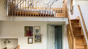 Un espace de vie de style loft avec un escalier en bois, un canapé en cuir noir agrémenté de coussins à motifs et des œuvres d’art accrochées aux murs.