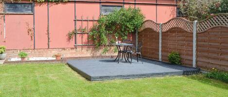 A red building with a tiled roof, a fenced garden, and a patio with a table and chairs.