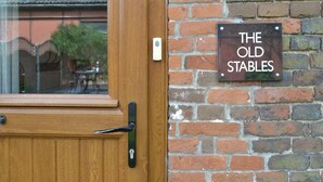 A wooden door with a brass handle and a glass window. A brick wall with a sign that reads "THE OLD STABLES" is visible. - 1 bedroom accommodation in Cantley, near Acle (Cantley, near Acle)
