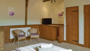 A hotel room with a bed, two wicker chairs, a wooden desk, a television, and a door. - 1 bedroom accommodation in Cantley, near Acle (Cantley, near Acle)